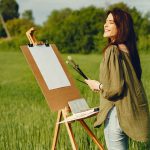 Frau stehe vor Staffelei und Leinwand und beginnt zu malen